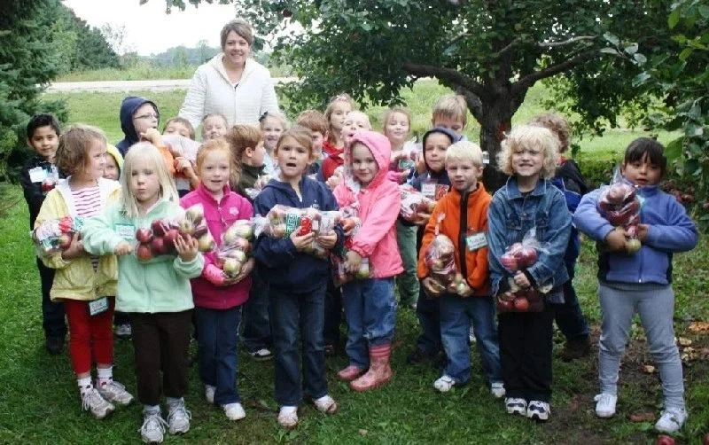 School group holding bags of freshly picked apples in the orchard